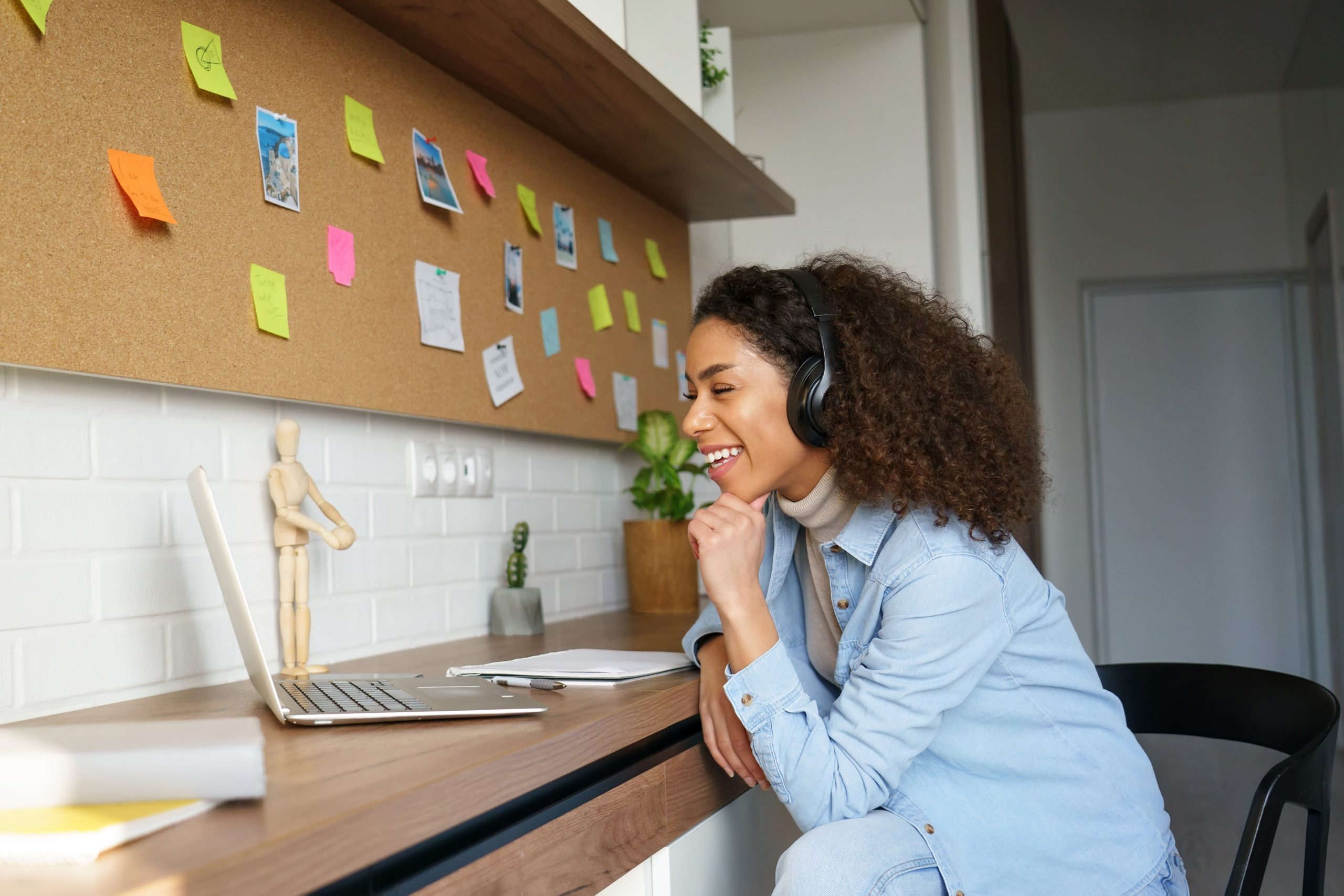 A smiling woman with long dark hair wearing a hands-free phone receiver, sat at a desk in front of a peg board covered with brightly coloured post-its.