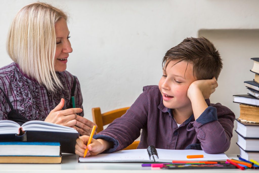 A tutor and young person sat at a desk with books piled on, engaged in conversation.