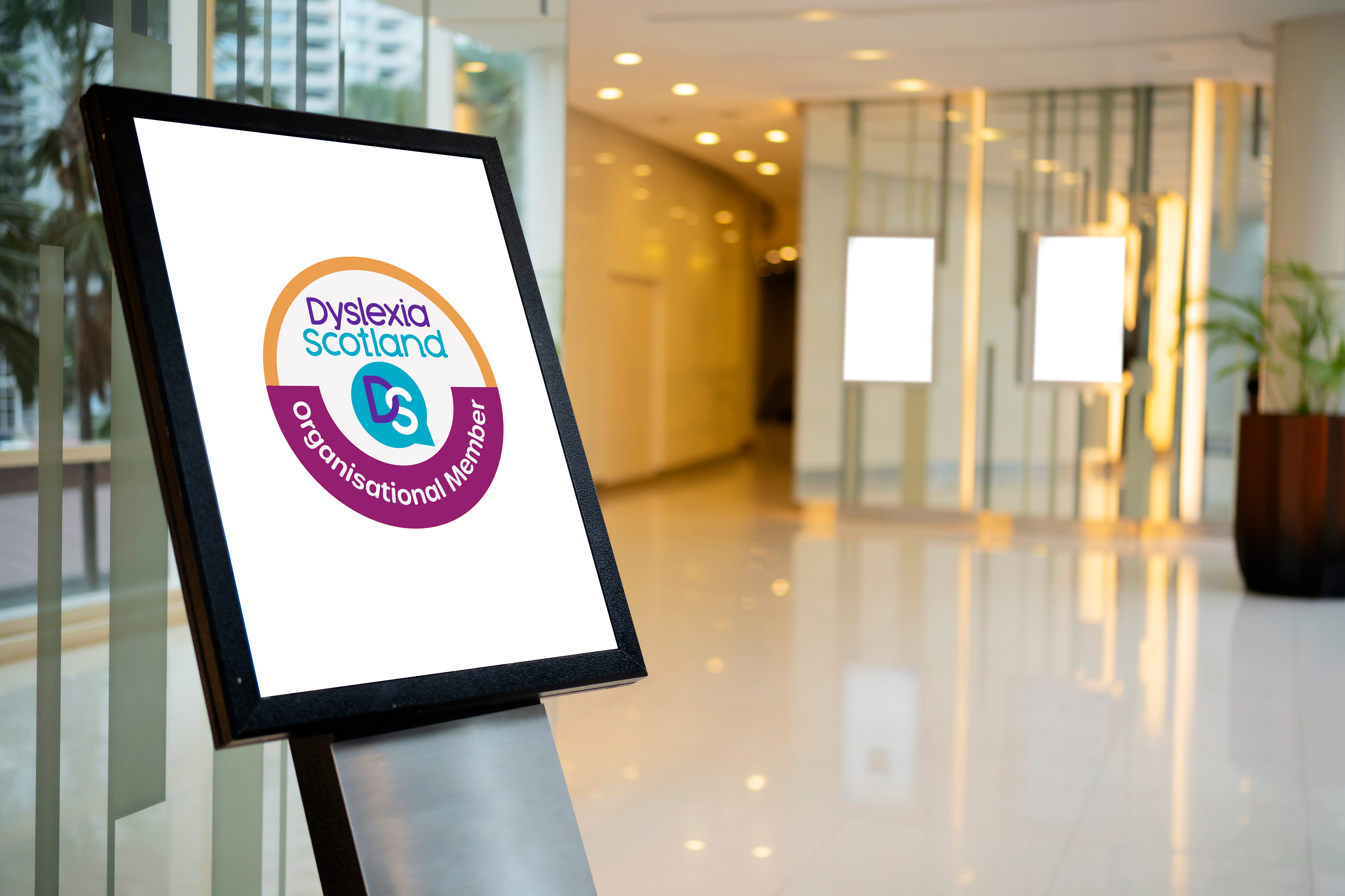 A digital Dyslexia Scotland membership badge displayed on a lecturn-style screen in a business reception area.