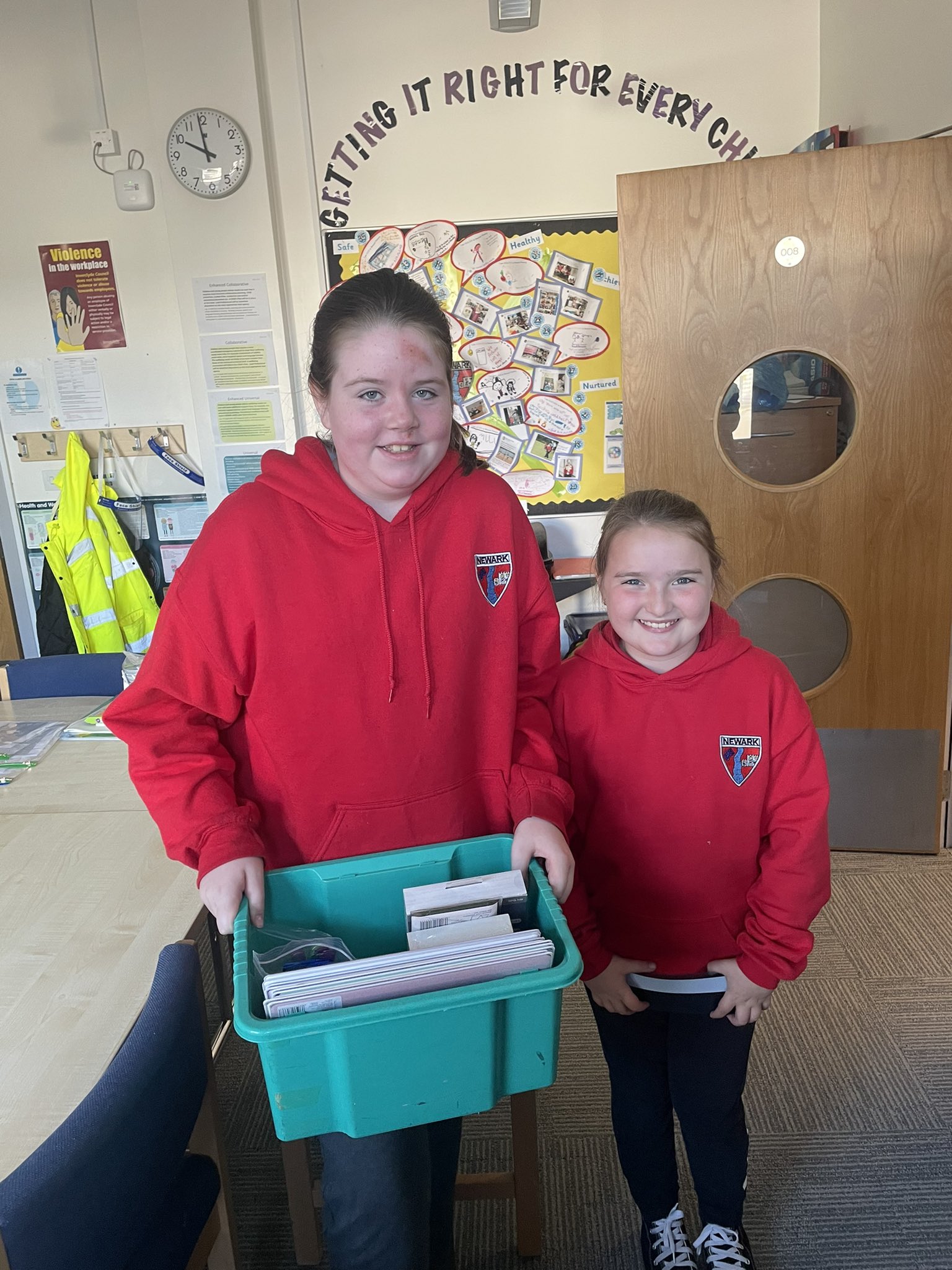 2 young people in red school uniform sweatshirts hold a box of dyslexia-friendly resources