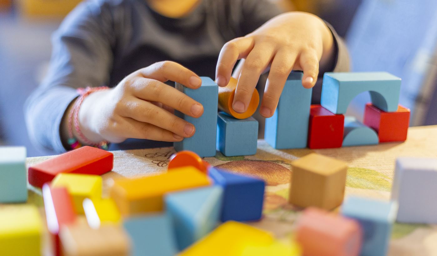 close up on a child's hands arranging coloured wooden building blocks