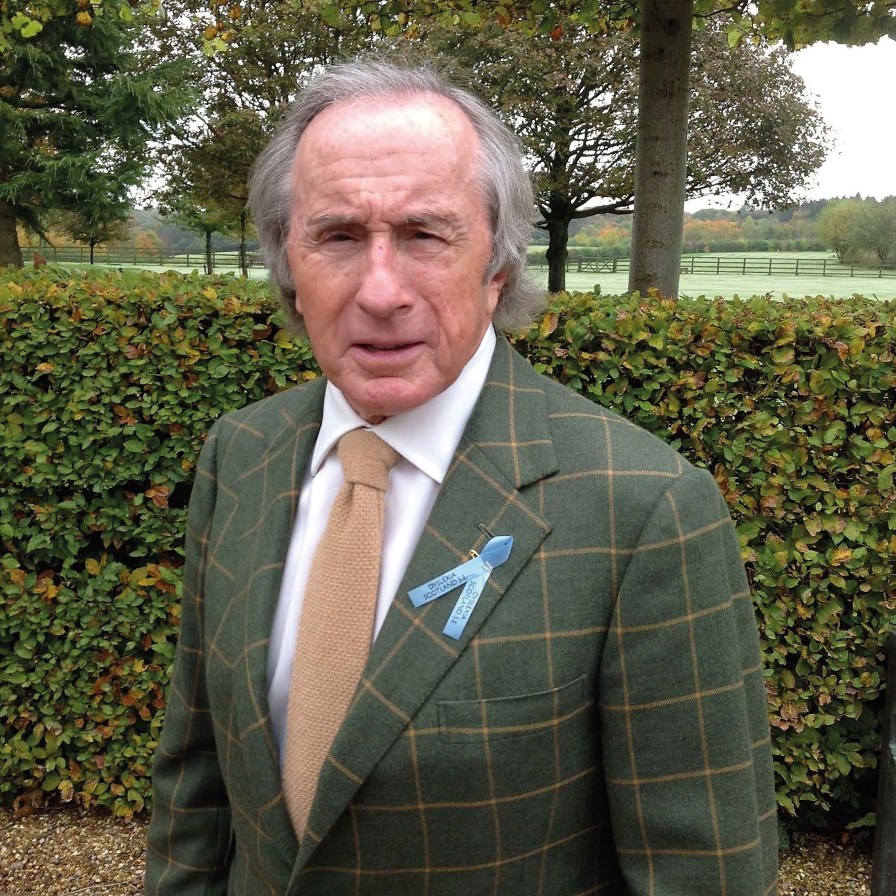 Sir Jackie Stewart in a green tweed suit with a blue ribbon on the lapel.