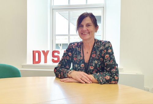 Dyslexia Scotland's new Volunteers Manager sits at a table in front of a window, smiling.