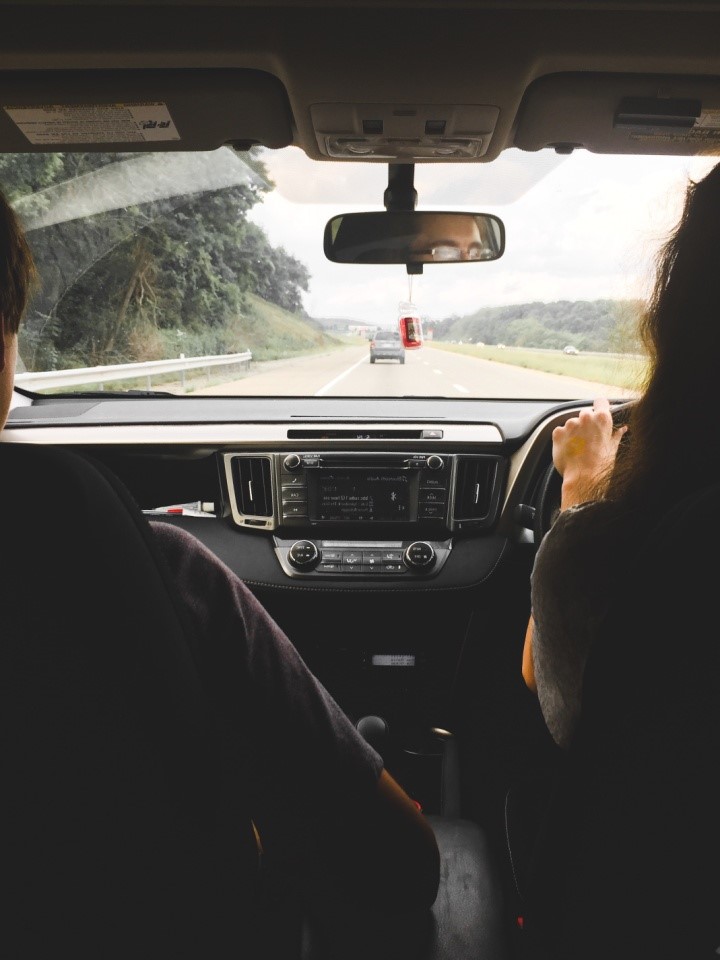 A view through a car windscreen from the back seat. The driver steers down an urban road.