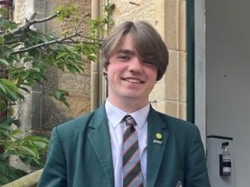 Monty wearing a green blazer and striped tie , smiles directly at us.