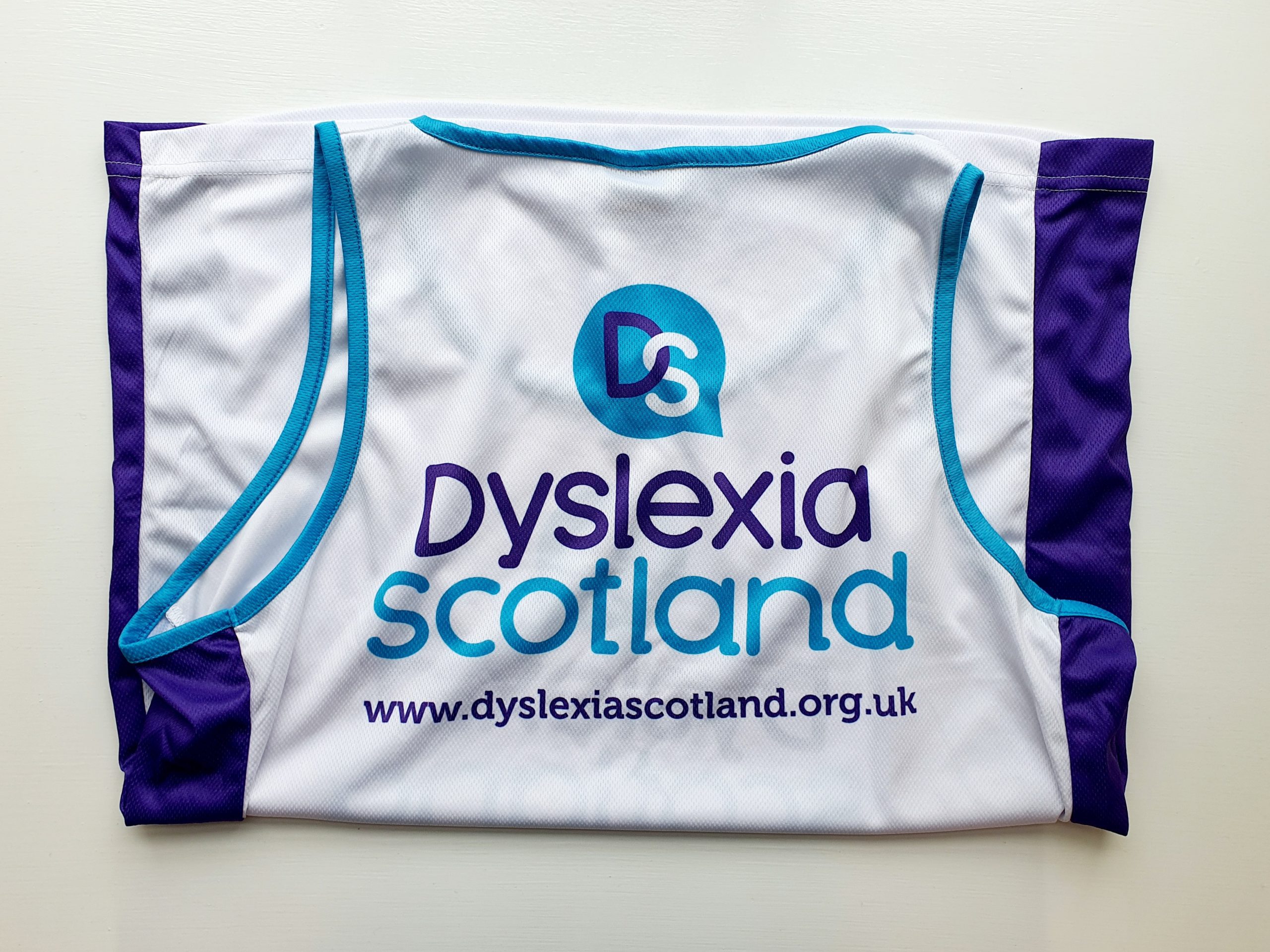 The vest folded so the back is showin g- the DYslexia Scotland logo is on the white back; the sides of the vest are purple panels.