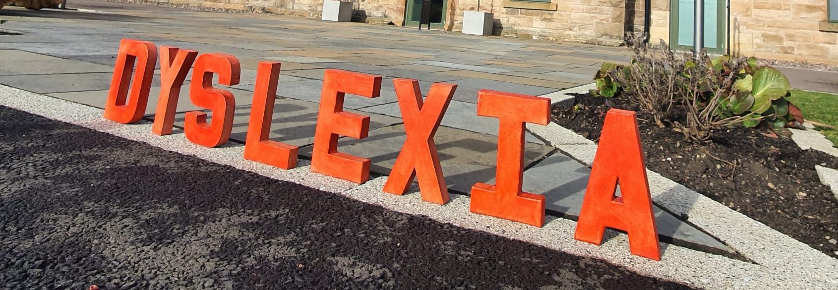 A worm's eye view of the front facade of Barracks Conference Centre, Stirling against a bright blue sky. The word 'dyslexia' is spelled out in red letters in the foreground.