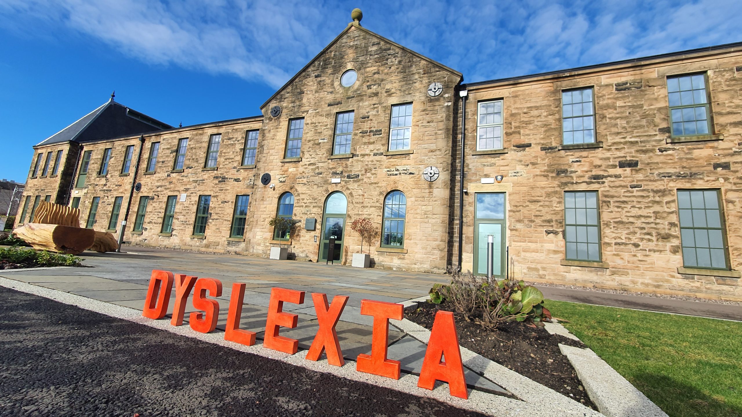 A worm's eye view of the front facade of Barracks Conference Centre, Stirling against a bright blue sky. The word 'dyslexia' is spelled out in red letters in the foreground.