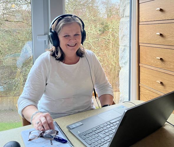 Volunteer wearing headphones using a laptop, smiles.