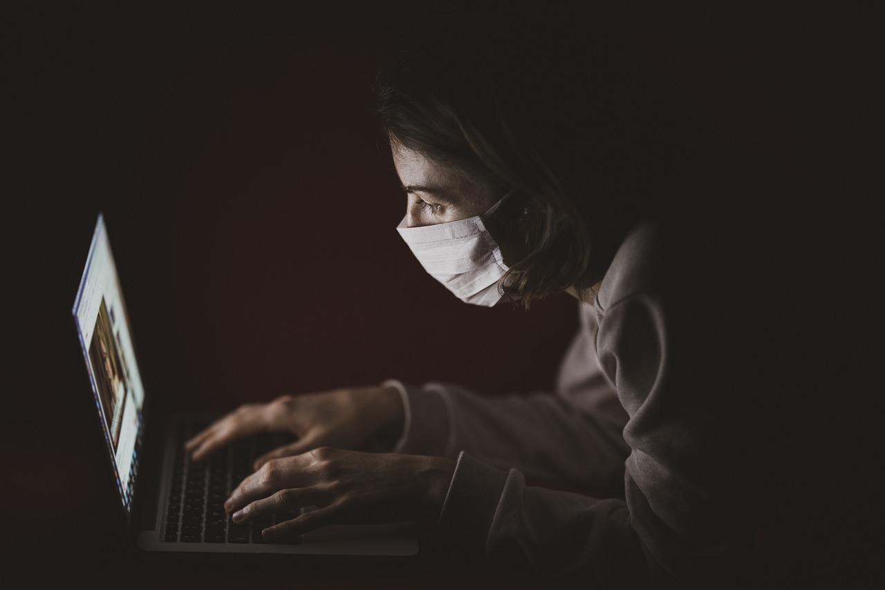 A student docto in a surgical masks leans in close to his laptop screen.