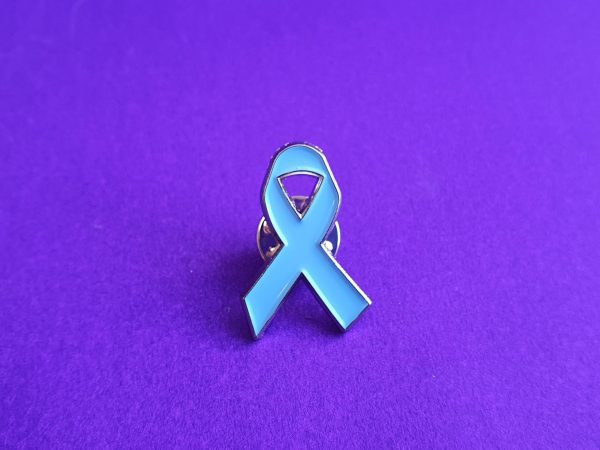 Pale blue charity ribbon pin badge placed against