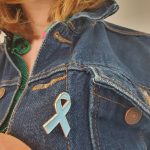 Pale blue dyslexia awareness ribbon pin badge shown on a denim jacket.