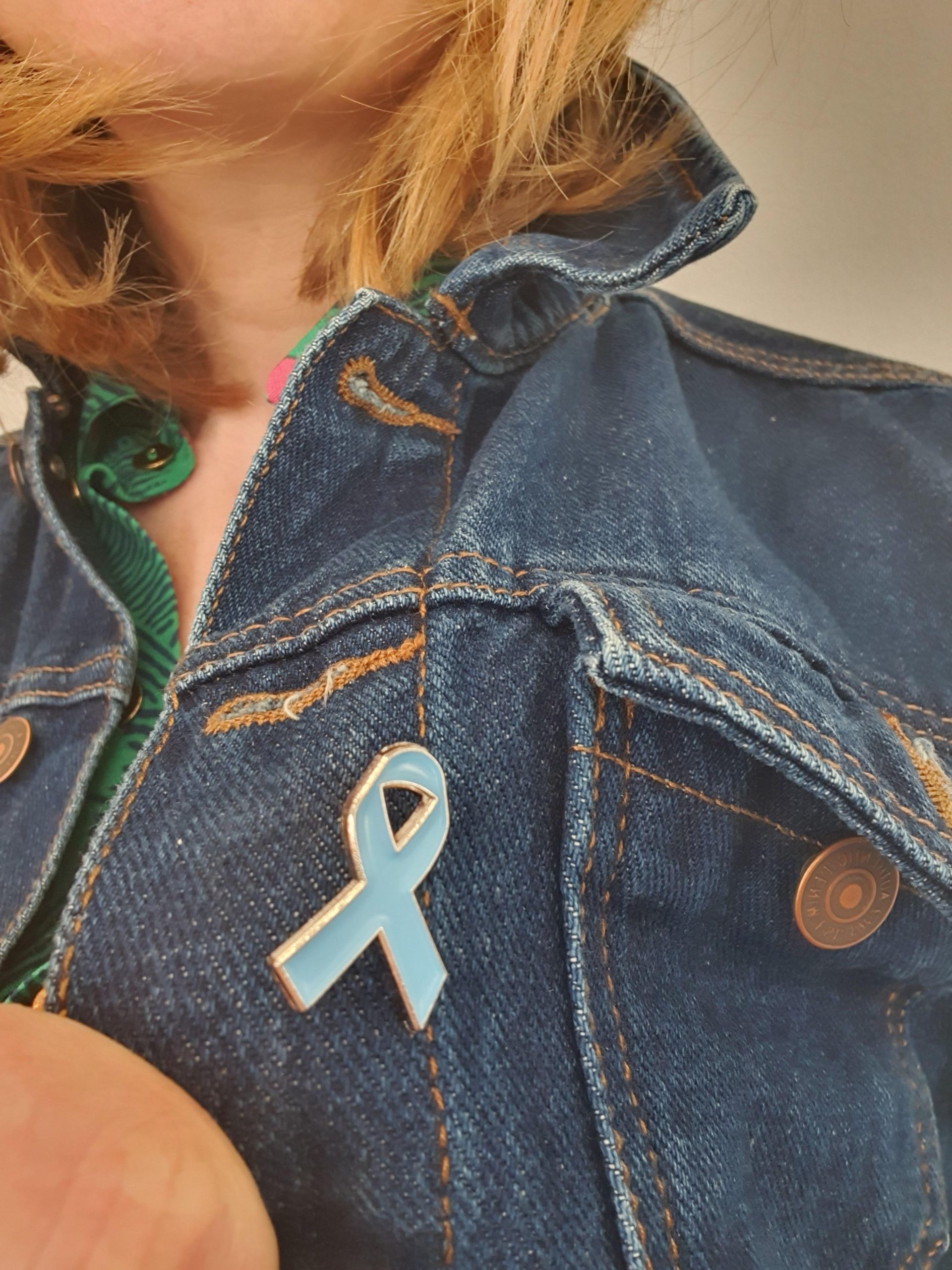 Pale blue dyslexia awareness ribbon pin badge shown on a denim jacket.