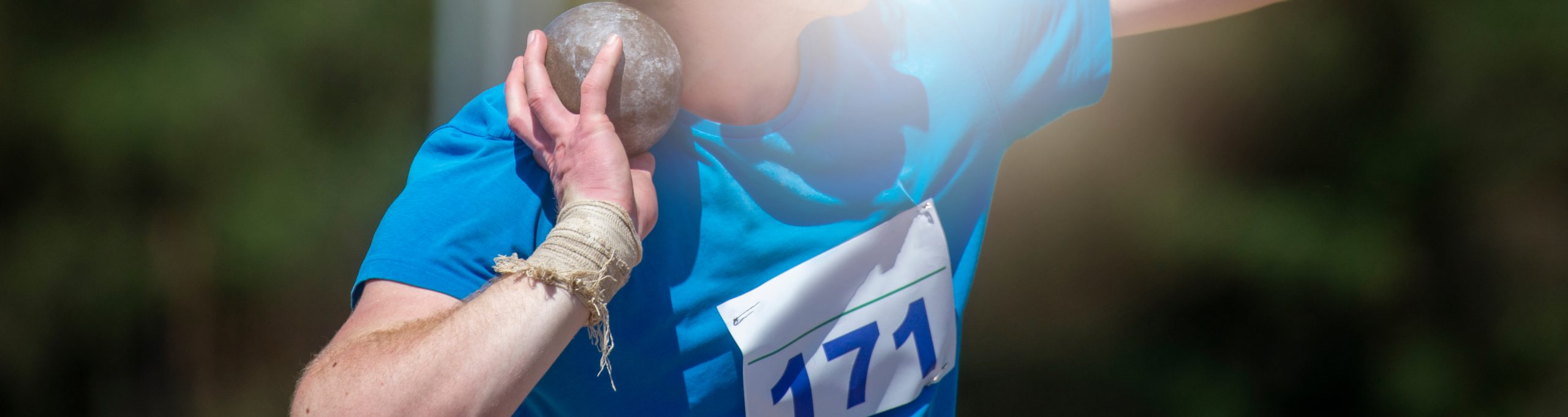 An athlete clutches a shotput to his neck; poised to toss it