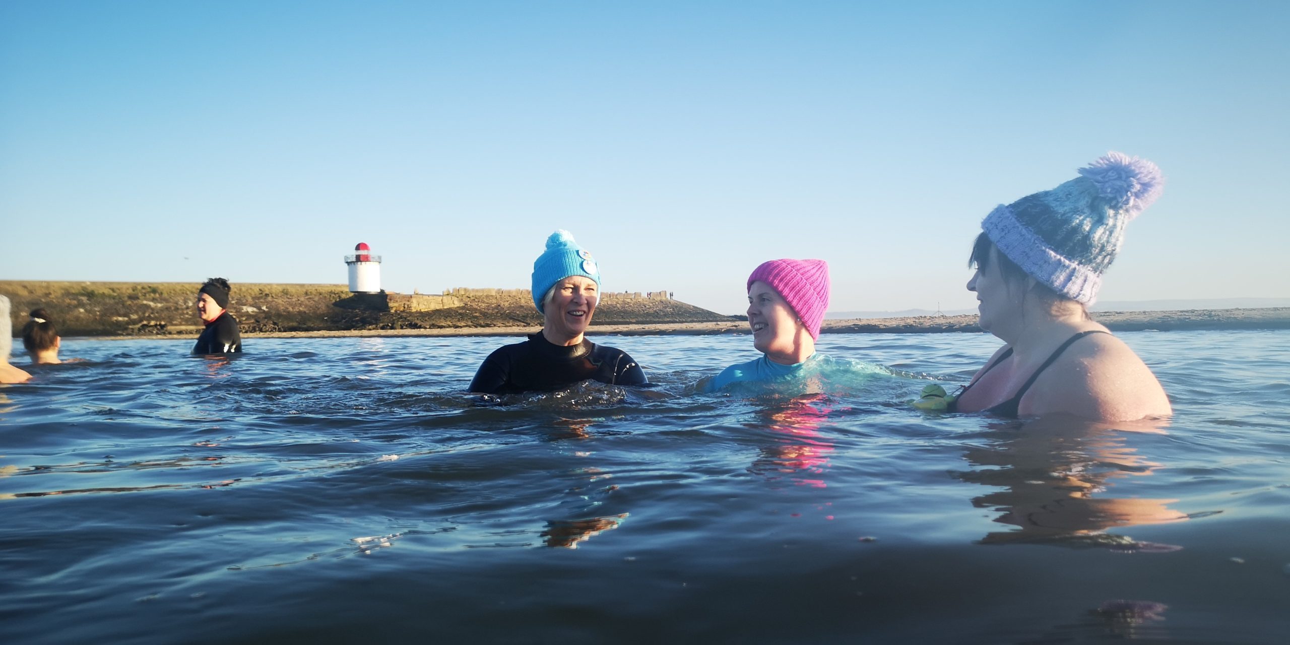 Wild swimmers bob in the water, wearing bobble hats.