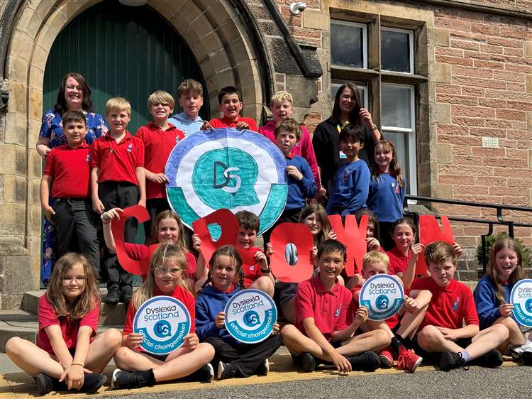 A large group on children in red polo shirts hold up hand-drawn changemaker badges.