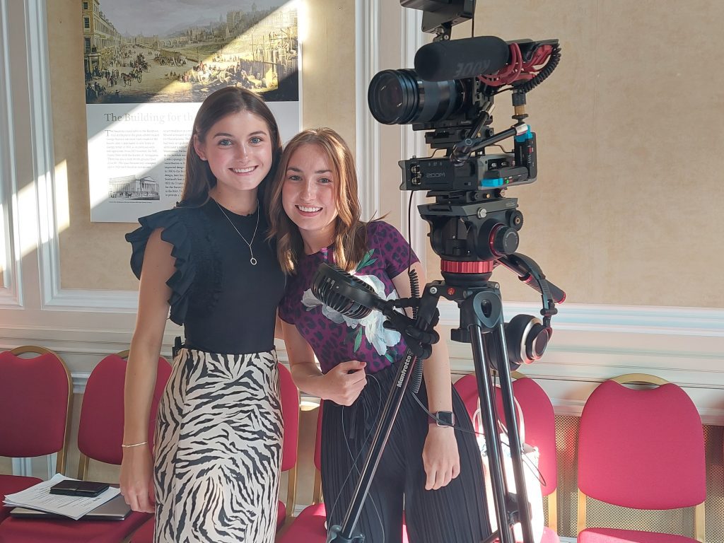 Two young women operate a professional film camera