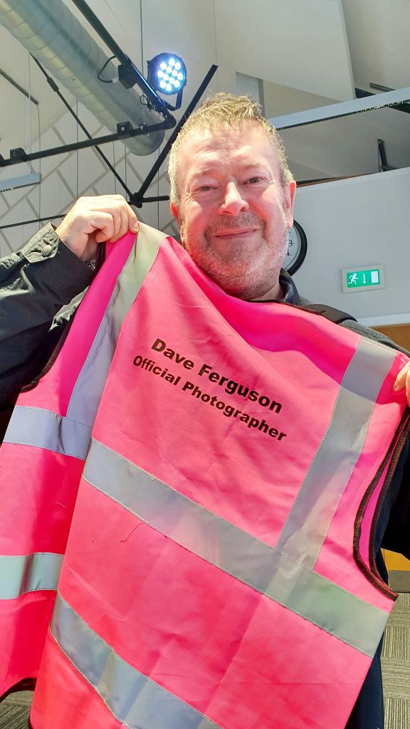 A photographer holds up his hi-vis vest