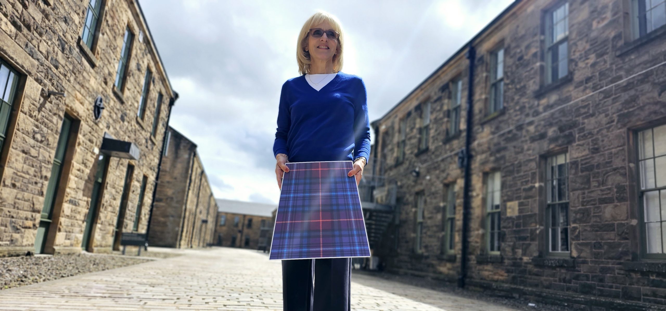 A woman holds up a cardboard kilt in an historic buildings complex