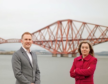 Two professionals stand in front of the Forth Road Rail Bridge.