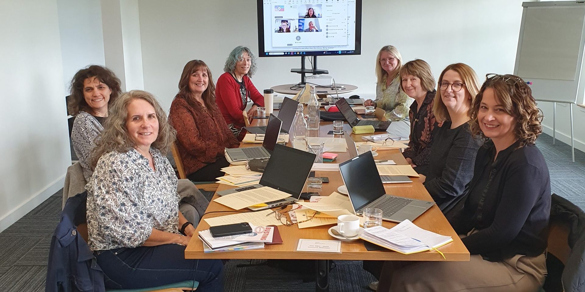 The group sit around a meeting table smiling.