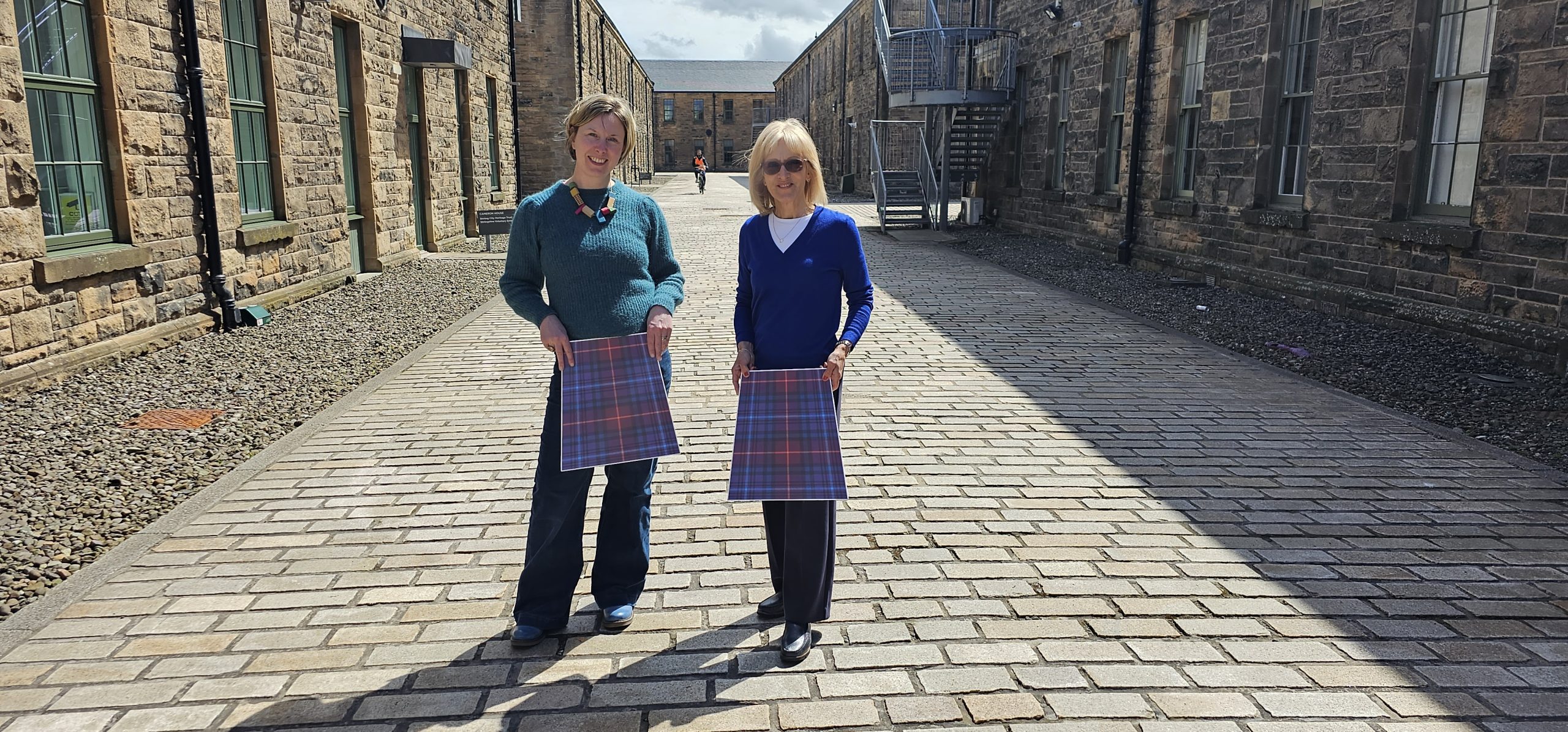 Two representatives of Dyslexia Scotland hold cardboard kitls to their waists in a historic setting